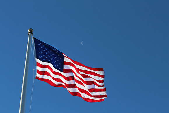 An American Flag Isolated on Blue Sky with Quarter Moon Peeking
